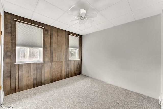 carpeted spare room featuring a drop ceiling, wood walls, and a ceiling fan