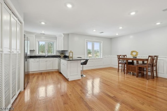 kitchen featuring white cabinetry, sink, light hardwood / wood-style flooring, kitchen peninsula, and plenty of natural light