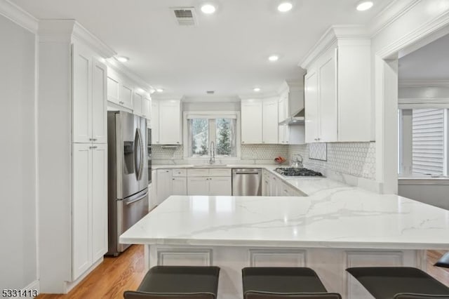 kitchen featuring a breakfast bar, kitchen peninsula, light stone countertops, white cabinetry, and stainless steel appliances