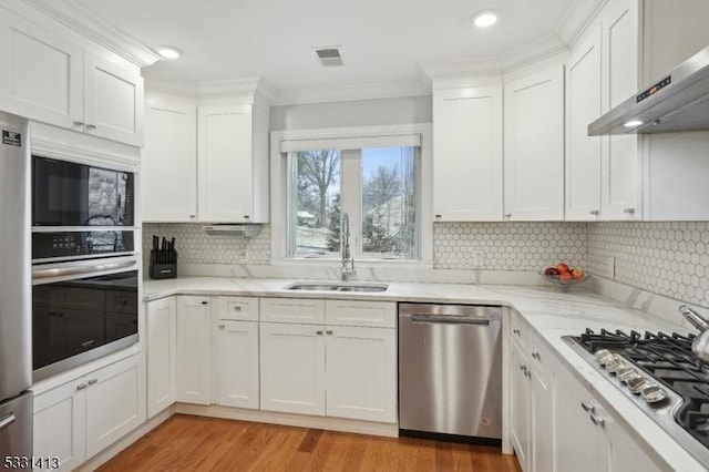 kitchen with light stone countertops, sink, stainless steel appliances, wall chimney range hood, and white cabinets