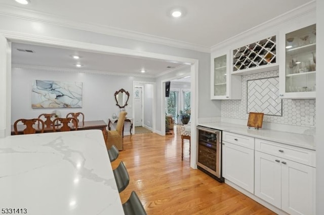 kitchen with light stone countertops, beverage cooler, crown molding, light hardwood / wood-style floors, and white cabinets