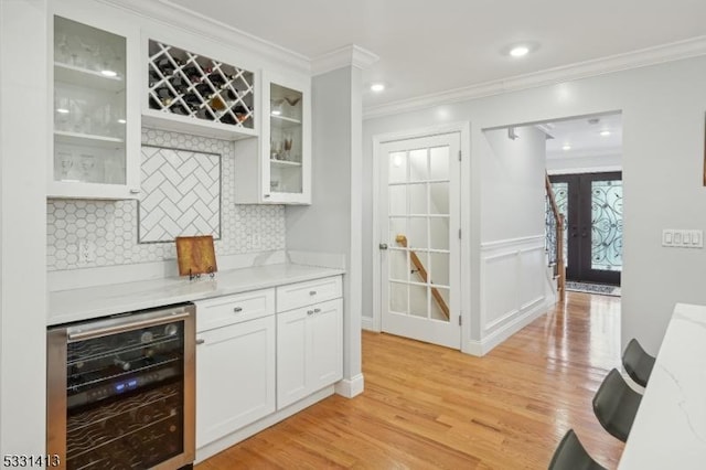 interior space featuring white cabinetry, french doors, beverage cooler, light stone counters, and crown molding