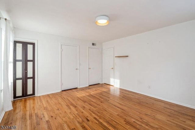 unfurnished bedroom featuring light hardwood / wood-style floors and two closets