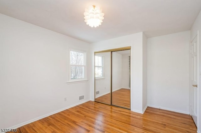 unfurnished bedroom featuring a notable chandelier, light wood-type flooring, and a closet