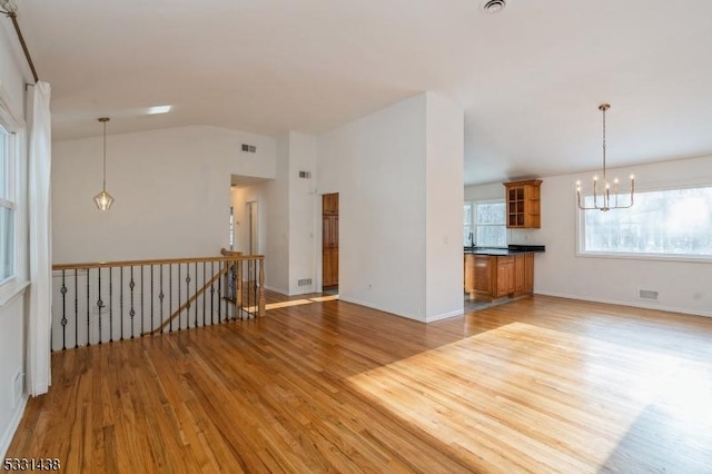 unfurnished living room featuring light wood-type flooring, vaulted ceiling, and a notable chandelier