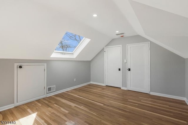 bonus room featuring vaulted ceiling with skylight, visible vents, baseboards, and wood finished floors