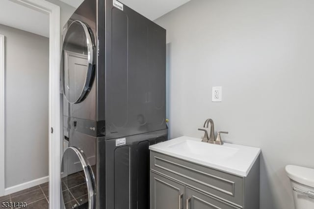 washroom with stacked washer / drying machine, a sink, laundry area, dark tile patterned floors, and baseboards