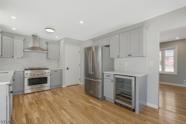 kitchen with wine cooler, high quality appliances, gray cabinets, wall chimney exhaust hood, and light wood finished floors