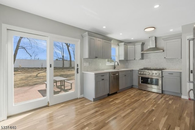 kitchen featuring gray cabinetry, stainless steel appliances, light countertops, light wood-type flooring, and wall chimney exhaust hood