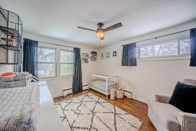 bedroom featuring hardwood / wood-style floors, ceiling fan, a baseboard heating unit, and a nursery area