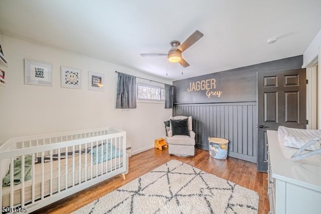 bedroom featuring ceiling fan, a crib, and hardwood / wood-style flooring