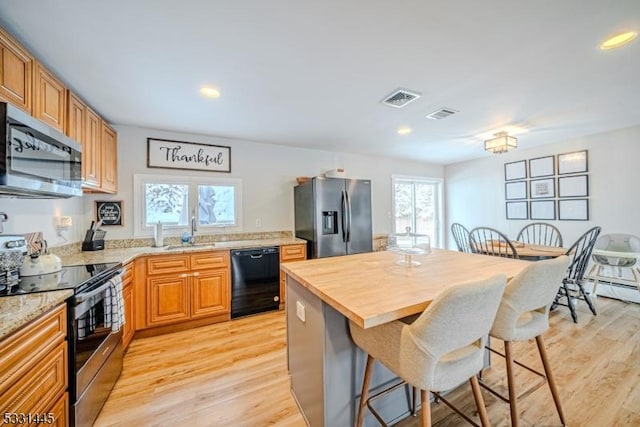 kitchen with a kitchen breakfast bar, sink, light wood-type flooring, and stainless steel appliances