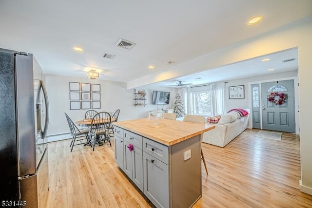 kitchen with gray cabinetry, a center island, wooden counters, a kitchen bar, and stainless steel refrigerator