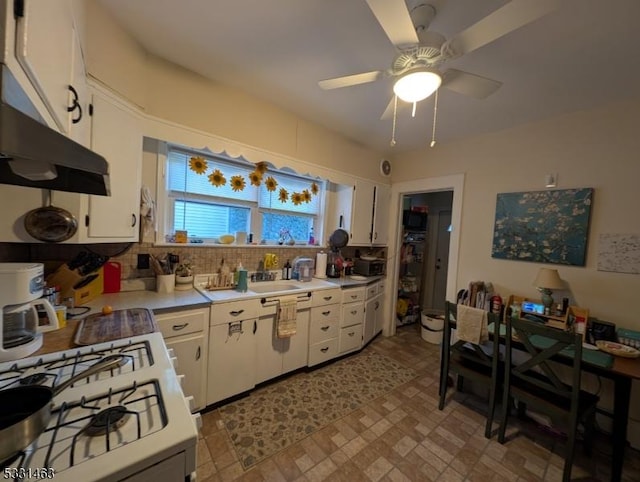 kitchen with backsplash, sink, ceiling fan, gas range gas stove, and white cabinetry