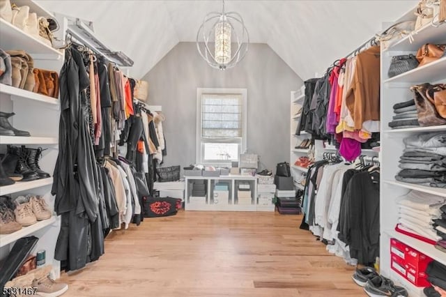 walk in closet with vaulted ceiling, an inviting chandelier, and light wood-type flooring