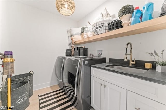 clothes washing area featuring sink, light hardwood / wood-style flooring, washing machine and dryer, and cabinets