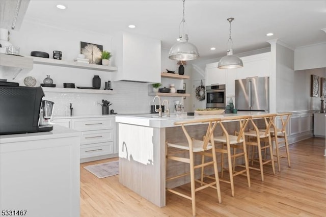 kitchen with a breakfast bar, white cabinetry, a center island with sink, appliances with stainless steel finishes, and backsplash