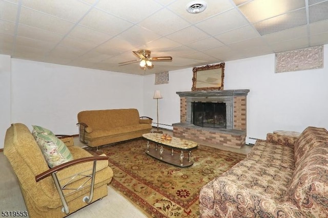 living room featuring a paneled ceiling, ceiling fan, a baseboard radiator, and a brick fireplace