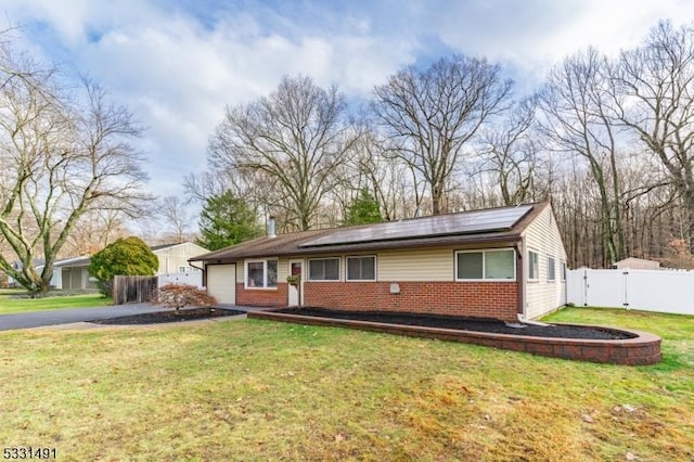 ranch-style home with a garage, a front yard, and solar panels