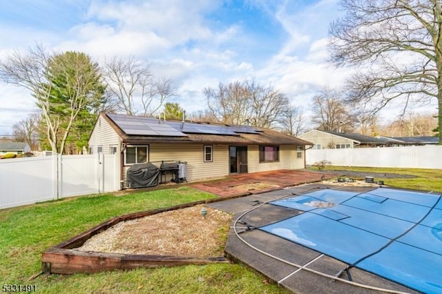 back of property with a lawn, solar panels, a patio area, and a covered pool