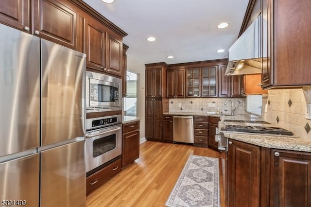 kitchen with sink, light hardwood / wood-style flooring, backsplash, custom range hood, and appliances with stainless steel finishes