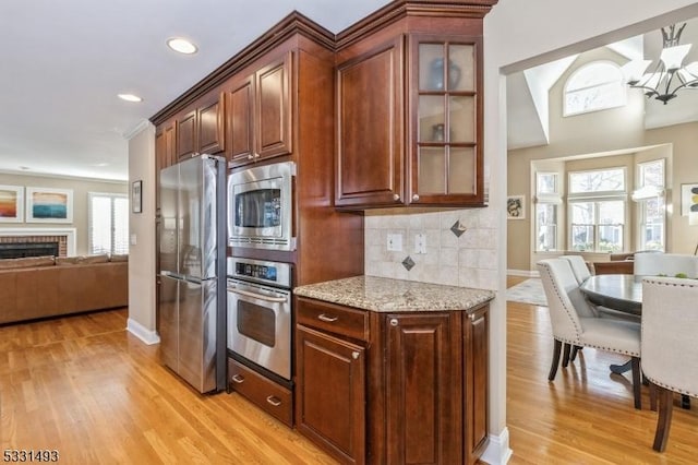 kitchen with decorative backsplash, light stone countertops, light wood-type flooring, stainless steel appliances, and a fireplace