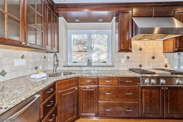 kitchen featuring sink, light stone counters, range hood, backsplash, and appliances with stainless steel finishes