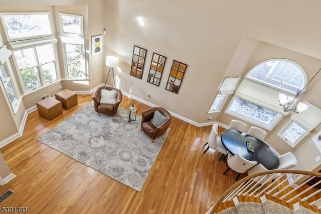 living area featuring wood-type flooring, a towering ceiling, and an inviting chandelier