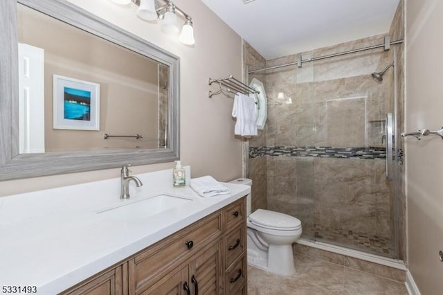 bathroom with a tile shower, vanity, toilet, and tile patterned floors