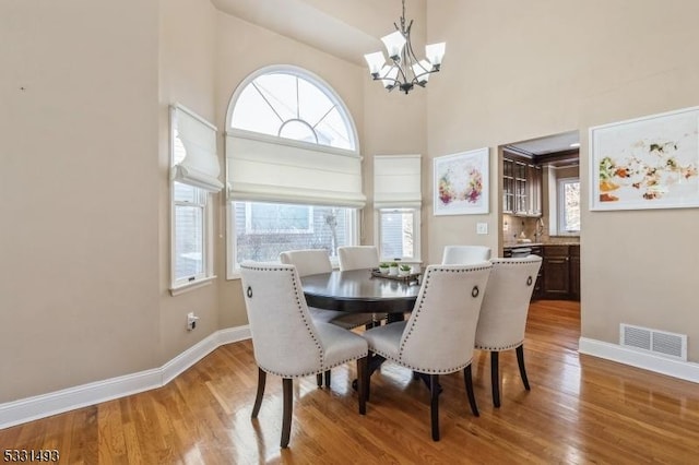 dining room featuring wood-type flooring, a notable chandelier, and a high ceiling