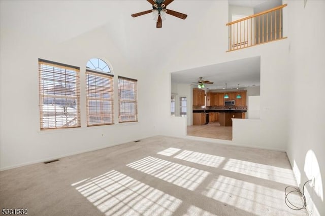 unfurnished living room with a towering ceiling, light carpet, and ceiling fan