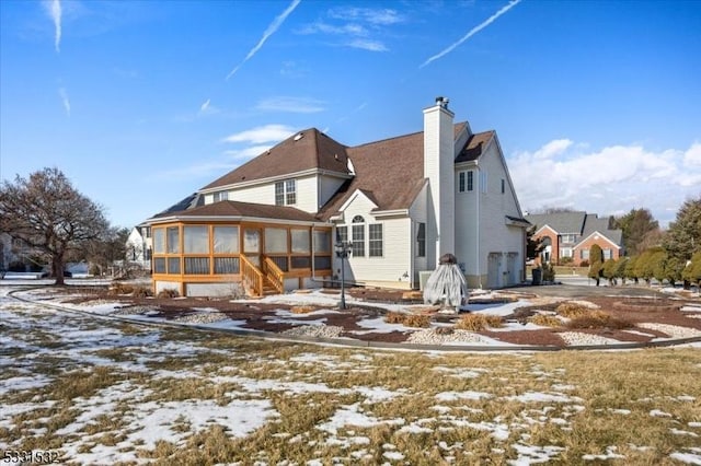 snow covered back of property with a sunroom