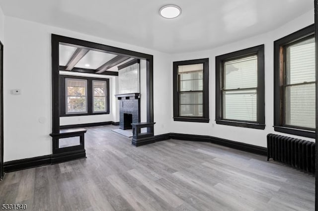 interior space featuring beam ceiling, radiator heating unit, light hardwood / wood-style floors, and a brick fireplace