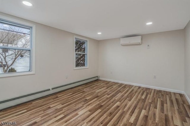 unfurnished room featuring a wall unit AC, hardwood / wood-style floors, and baseboard heating