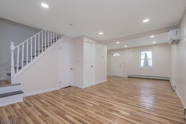 unfurnished living room featuring baseboard heating, light hardwood / wood-style floors, and a wall mounted air conditioner