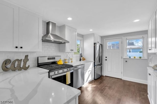 kitchen featuring wall chimney exhaust hood, light stone counters, appliances with stainless steel finishes, dark hardwood / wood-style flooring, and white cabinetry