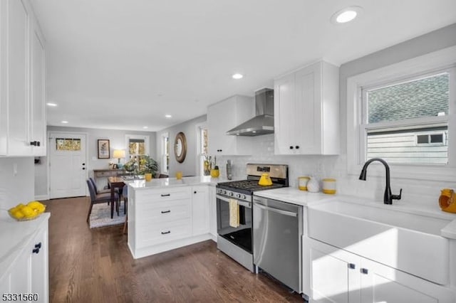 kitchen featuring white cabinets, wall chimney exhaust hood, dark hardwood / wood-style flooring, kitchen peninsula, and stainless steel appliances