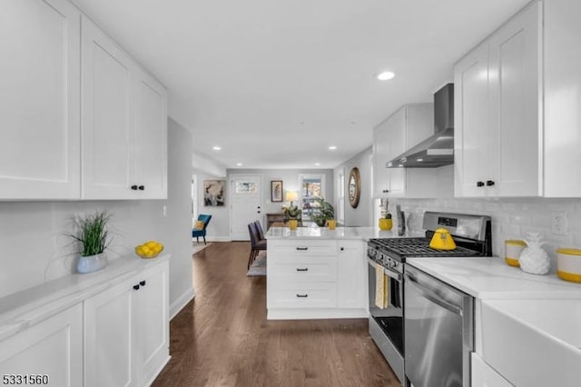 kitchen with white cabinets, wall chimney range hood, kitchen peninsula, and appliances with stainless steel finishes