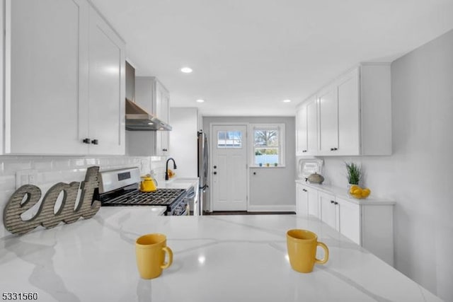 kitchen featuring white cabinetry, light stone counters, wall chimney exhaust hood, and range