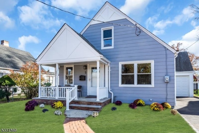 bungalow-style house featuring a porch, a garage, an outbuilding, and a front lawn