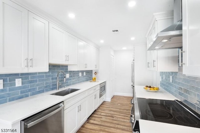 kitchen featuring appliances with stainless steel finishes, wall chimney exhaust hood, sink, light hardwood / wood-style flooring, and white cabinets