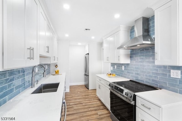 kitchen with white cabinetry, sink, stainless steel appliances, and wall chimney range hood