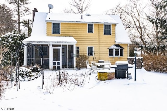 snow covered house featuring a sunroom and a chimney