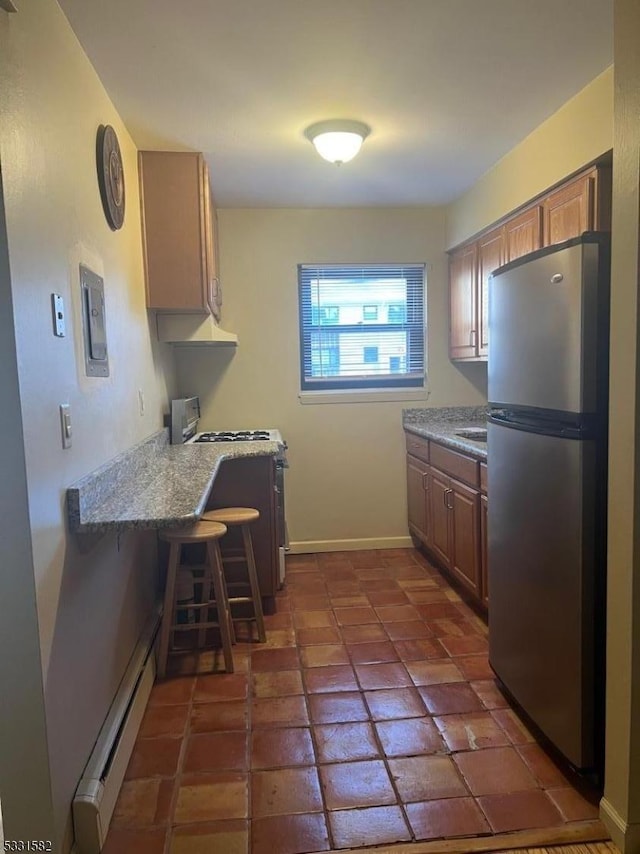 kitchen featuring a kitchen breakfast bar, stove, a baseboard heating unit, dark tile patterned flooring, and stainless steel refrigerator