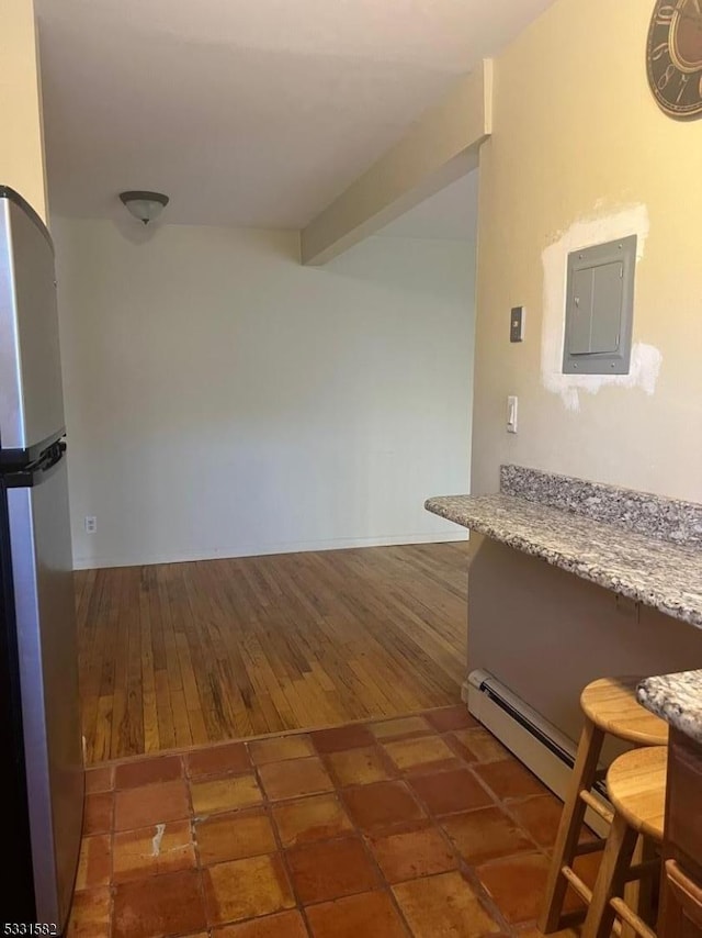 kitchen with stainless steel refrigerator, light stone countertops, beamed ceiling, a baseboard heating unit, and electric panel