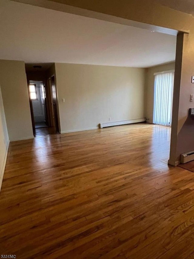 unfurnished living room with a baseboard heating unit and dark wood-type flooring