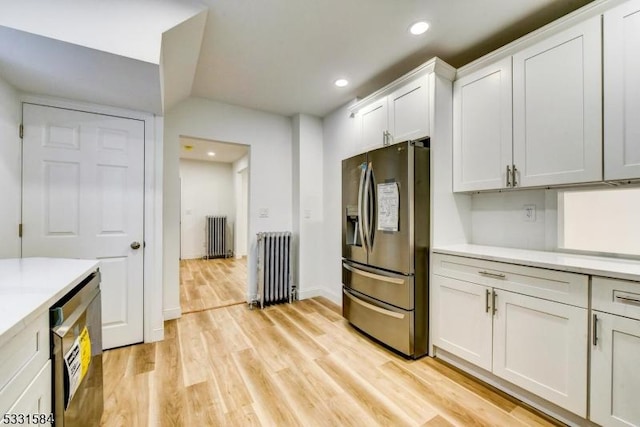 kitchen featuring appliances with stainless steel finishes, radiator, light hardwood / wood-style flooring, and white cabinets