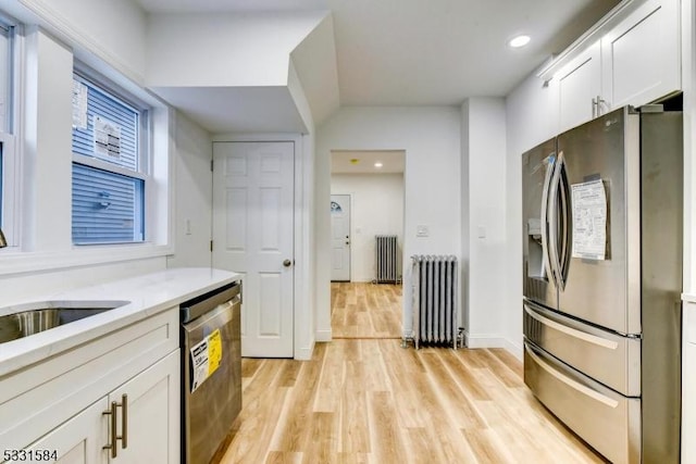 kitchen featuring appliances with stainless steel finishes, radiator heating unit, light wood-type flooring, and white cabinets