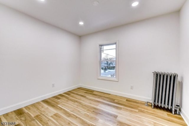 spare room featuring radiator and light hardwood / wood-style flooring