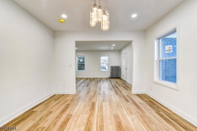 unfurnished living room with an inviting chandelier, radiator, and light hardwood / wood-style flooring